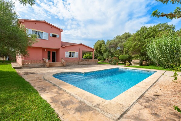 Une maison à deux étages avec une piscine, entourée d’une pelouse bien entretenue et d’arbres.