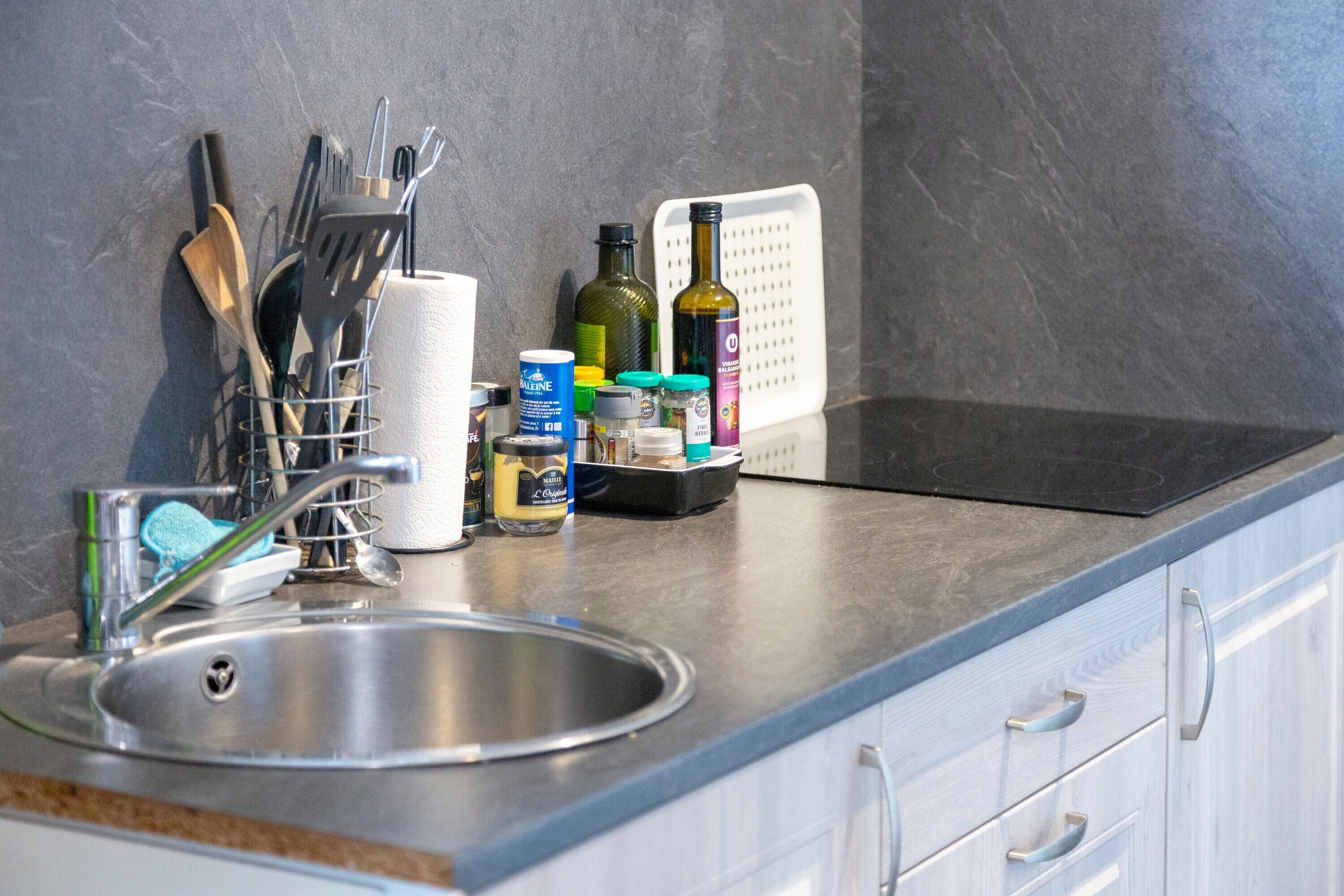 A kitchen with a stainless steel sink, a dish rack, and various kitchen utensils and appliances.