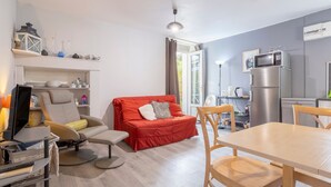 A modern living area with a sofa, a dining table, and a kitchen area with a refrigerator and microwave.