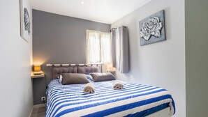 A bedroom with a bed, a nightstand, a window with curtains, and a wall-mounted artwork.