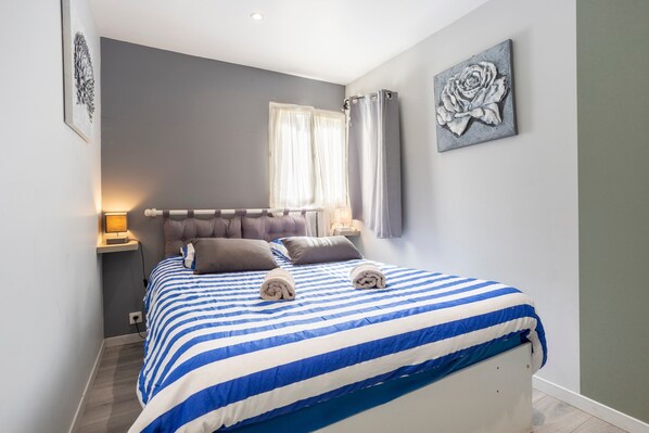 A bedroom with a bed, a nightstand, a window with curtains, and a wall-mounted artwork. - Holiday Apartment L'Eclose Ty Gwen with Private Terrace, Shared Garden – Bike-Friendly & Near GR34 (Guilvinec)