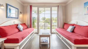 Ein Zimmer mit zwei roten Sofas, einem kleinen Tisch und Blick durch eine Glastür.
