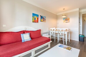 Una habitación con un sofá rojo, una mesa de comedor blanca con sillas y cuadros en la pared.