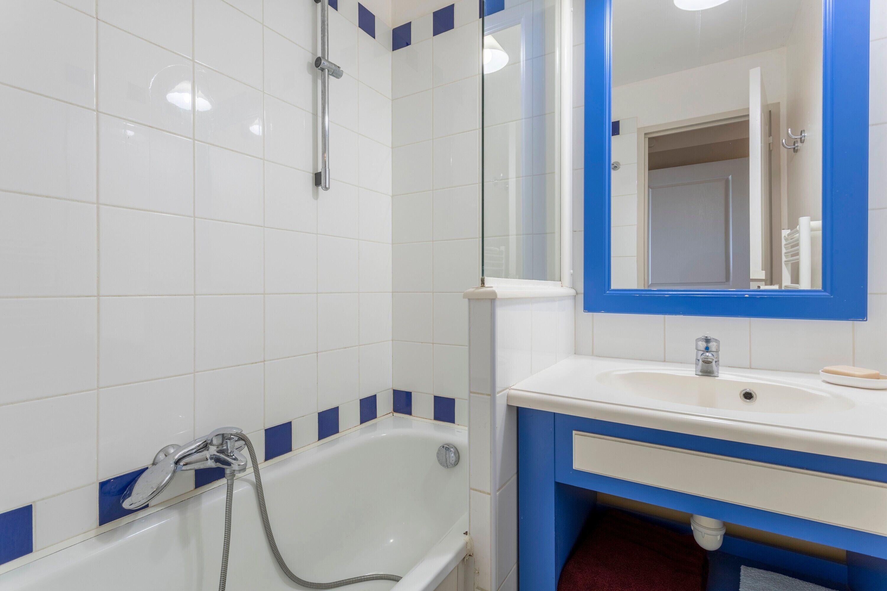 Ein Badezimmer mit einer weißen Badewanne, einem blauen Duschbereich, einem weißen Waschbecken mit Spiegel und einem roten Handtuch auf dem Boden.
