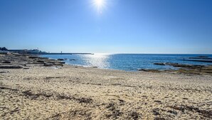 Ein Strand mit blauem Himmel, ruhigem Wasser und Felsformationen.