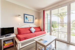 Una habitación con un sofá rojo, un televisor sobre una mesita auxiliar y una mesa con una revista.