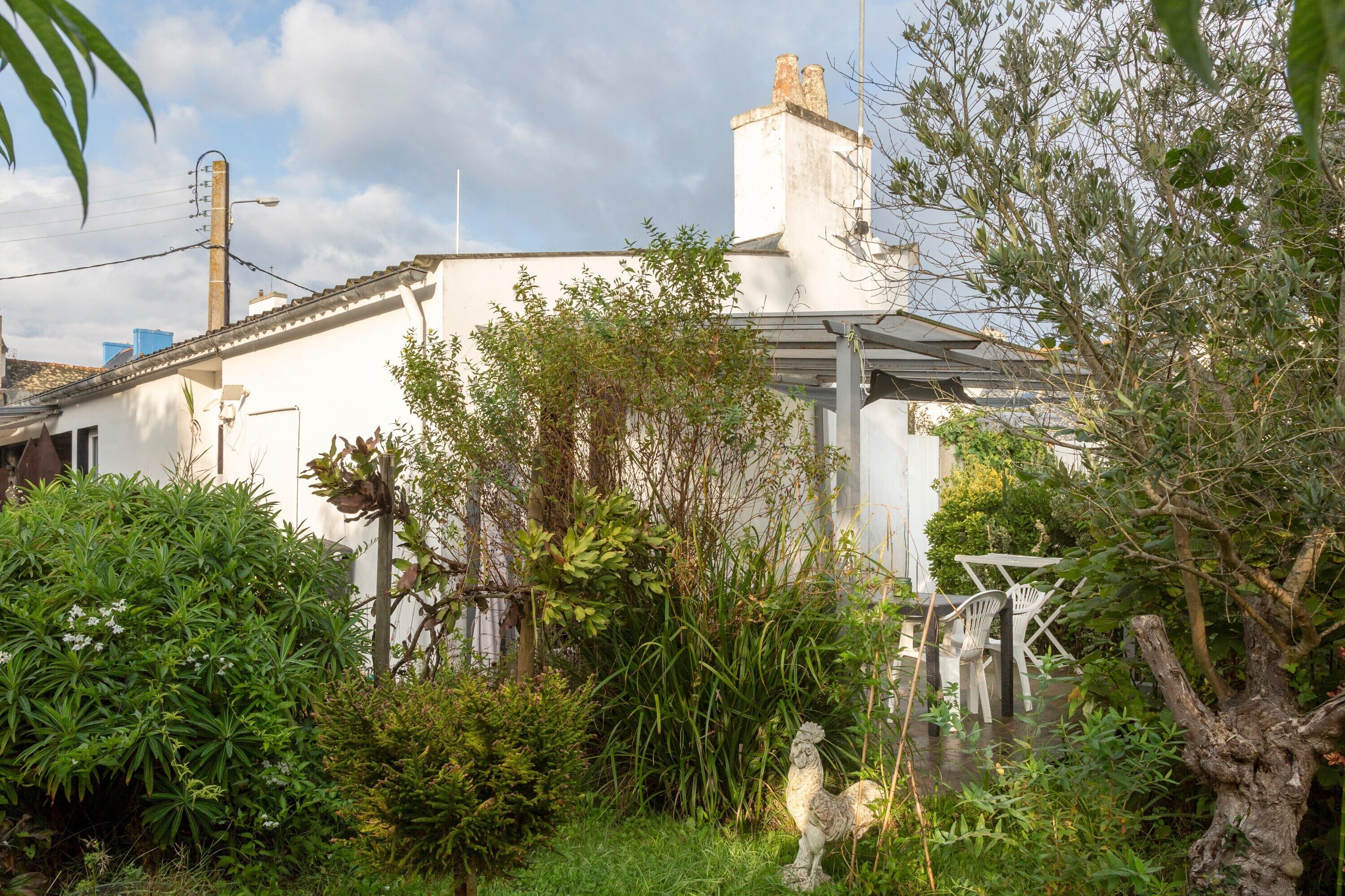 Ein weißes Gebäude mit Gartenanlage, darunter eine Statue und Sitzmöglichkeiten im Freien.