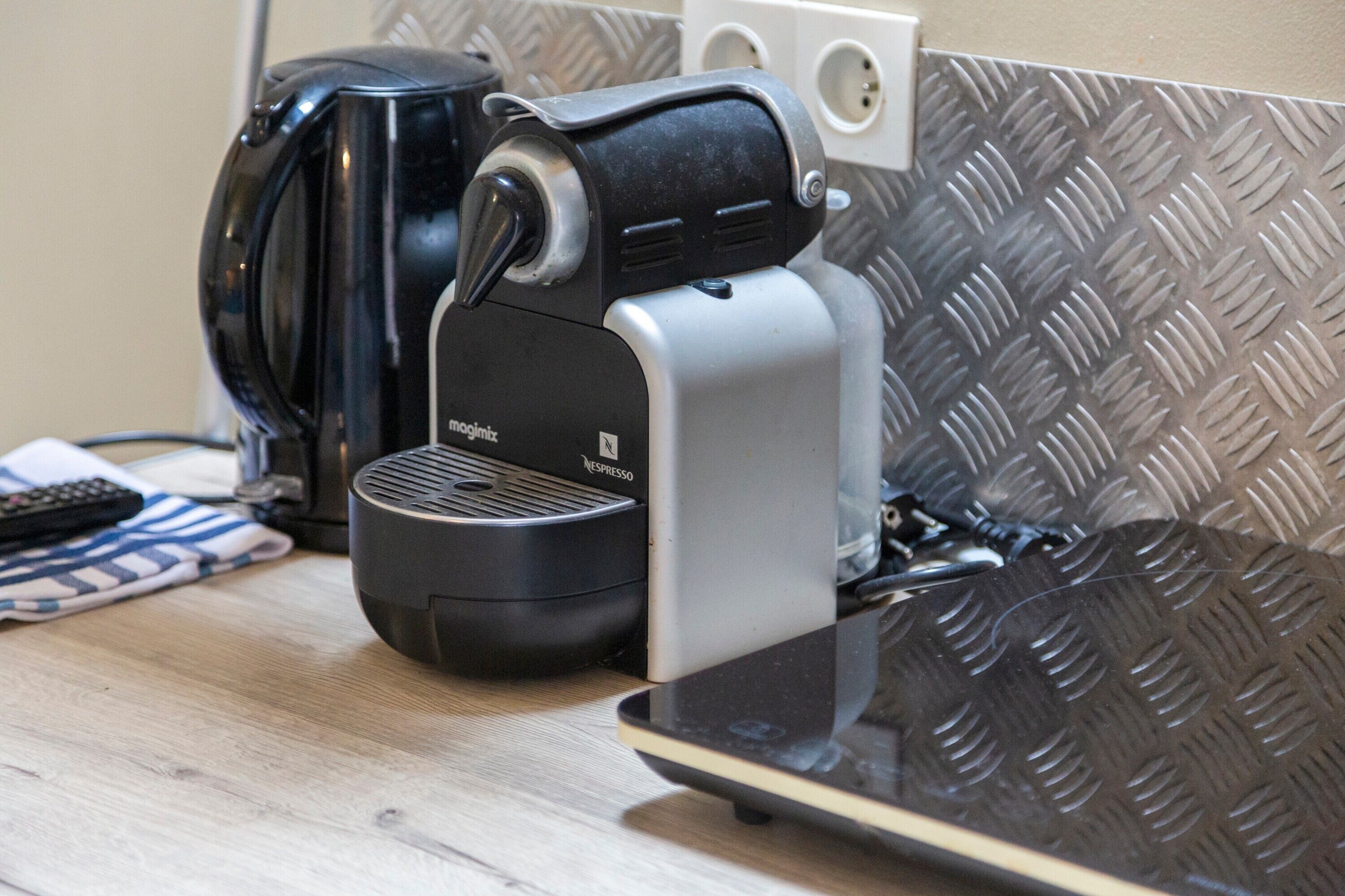 A coffee maker with a pod dispenser, a remote control, and a power outlet on a wooden surface.