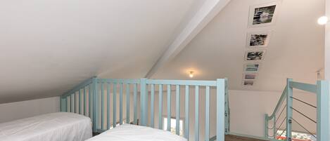 Un dormitorio con dos camas, un tragaluz, una escalera y vistas al exterior.