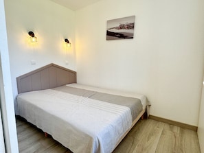 Ein Einzelbett mit Kopfteil, zwei Wandlampen und ein gerahmtes Bild an der Wand.