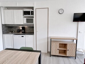 Eine kleine Küche mit weißen Schränken, einer Mikrowelle, einer Kaffeemaschine und einer Uhr an der Wand.