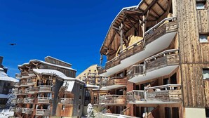 A snow-covered ski resort with wooden buildings featuring balconies and ski lifts.