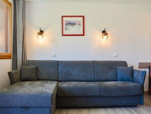 Ein Wohnzimmer mit einem grauen Sofa, zwei Wandleuchten und einem gerahmten Bild an der Wand.