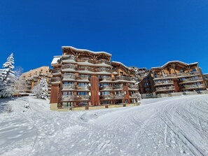 A multi-story wooden building with balconies, surrounded by snow-covered trees.