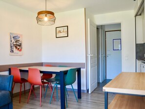 A dining area with a wooden table and colorful chairs, a hanging light fixture, and a door leading to another room.