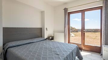 Ein Schlafzimmer mit einem Bett, einem Heizkörper, einem Fenster mit Vorhängen und Blick ins Freie.