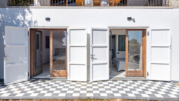 A building with two open doors leading to a room with a bed and a table. - Holiday Home 'Ami' with Sea View, Private Terrace and Shared Garden (Arzana)