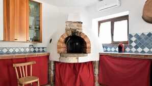 A kitchen with a brick oven, wooden cabinets, and a red chair. - Holiday Home 'Ami' with Sea View, Private Terrace and Shared Garden (Arzana)