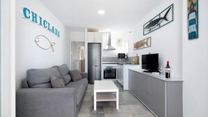 A compact living space with a kitchenette, a grey sofa, a white coffee table, and a TV.