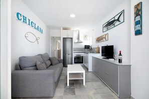 A compact living space with a kitchenette, a grey sofa, a white coffee table, and a TV.