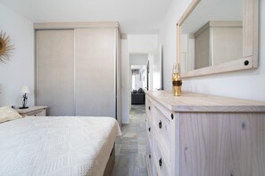 Un dormitorio con cama, cómoda, espejo, lámpara y un pasillo que conduce a otra habitación.