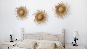 A bedroom with a wooden headboard, two bedside tables with lamps, a bed with patterned pillows, and three wall-mounted sun hats.