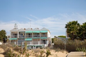 Un hotel frente a la playa con varios balcones, una playa de arena y palmeras.