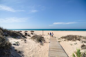 Una pasarela de madera que conduce a una playa con dunas y sombrillas.