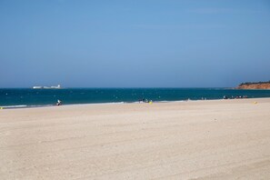 Une plage avec un ciel dégagé, une mer calme et une côte lointaine.