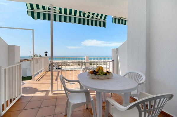 Une terrasse avec une table et des chaises, un panier de fruits et une vue sur la mer.