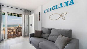 A modern living room with a grey sofa, a white coffee table, and a view of the sea through a glass door.