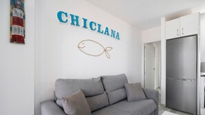 A modern living room with a grey sofa, a wall-mounted fish decoration, and a stainless steel refrigerator.