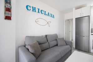 A modern living room with a grey sofa, a wall-mounted fish decoration, and a stainless steel refrigerator.