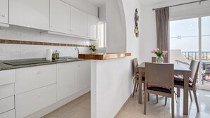 A modern kitchen with white cabinets, a wooden countertop, and a dining area with a table and chairs. - Holiday Apartment "Clementina Imperial Park" with Sea View, Shared Pool & Wi-Fi (Calp)