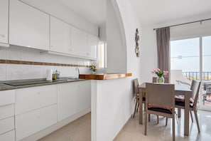 A modern kitchen with white cabinets, a wooden countertop, and a dining area with a table and chairs.