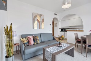 Ein modernes Wohnzimmer mit grauem Sofa, einem Couchtisch und einem Essbereich mit Stühlen und einem Tisch.