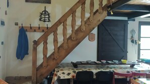 Un escalier avec des rampes en bois, une table à manger avec des chaises, un luminaire fixé au mur et un tableau.