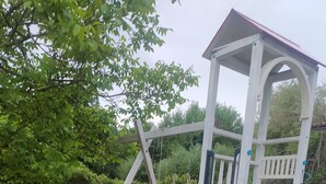 Une aire de jeux avec un toboggan vert, des balançoires jaunes et roses, et une structure d’escalade blanche.
