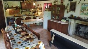 Une cuisine rustique avec des meubles en bois, une table à manger recouverte d’une nappe à motifs floraux et une cheminée.