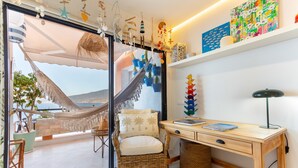 A room with a view of the sea, a hammock, wicker furniture, a desk, and decorative items.
