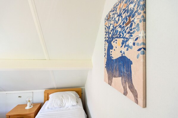 Un dormitorio con una cama, una mesita de noche y un cuadro colgado en la pared de un árbol y ciervos.
