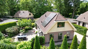 Ett bostadsområde med ett hus som har ett sluttande tak med solpaneler, och som omges av välskötta häckar och träd.