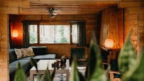 A cozy cabin interior with a wooden ceiling, a ceiling fan, a sofa, a coffee table, and two floor lamps. - Cozy and romantic forest house at Veluwe (Putten)