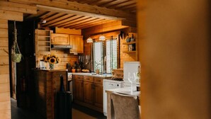 A wooden cabin kitchen with a central island, wooden cabinets, and a hanging pot rack. - Cozy and romantic forest house at Veluwe (Putten)