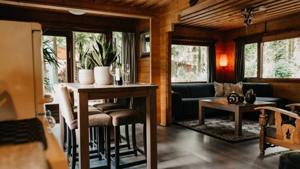 A cozy wooden interior with a dining area, sofa, and a table with a candle. - Cozy and romantic forest house at Veluwe (Putten)