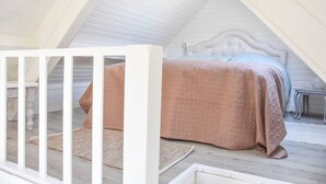 Ein Schlafzimmer im Dachgeschoss mit hohen Decken, einem geneigten Dach, einem weißen Babybett und einem Bett mit einer rosa Decke.