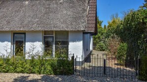 Ein Haus mit Strohdach, weißen Außenwänden und einem schwarzen Metallzaun.