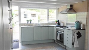 Eine Küche mit weißen Schränken, einem Gasherd und einem Fenster mit Blick auf einen Garten.