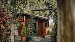 Een rustieke houten chalet met een groene deur, omgeven door dichte beplanting en plantenpotten.