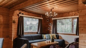 Een gezellig interieur van een chalet met houten plafond, een bank, een salontafel en twee ramen met gordijnen.